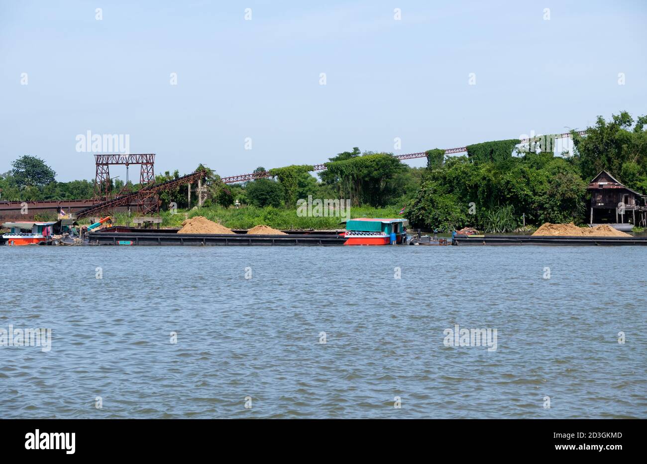 Das große Frachtschiff lädt den Sand für den Transport zur Baustelle, während es die verlassene Fabrik in der Nähe des großen Flusses passiert. Stockfoto