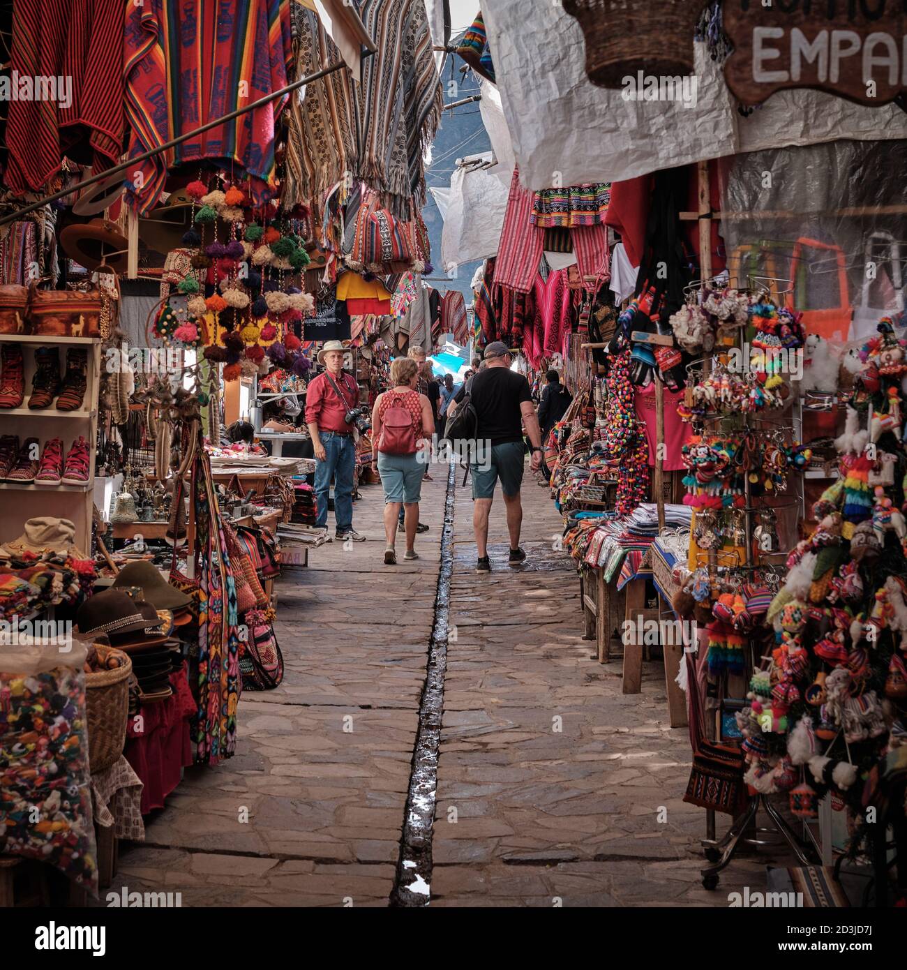 Touristen schlendern durch den Pisaq Markt, Pisac, Peru, umgeben von Souvenirs und Kleidung auf Marktständen Stockfoto