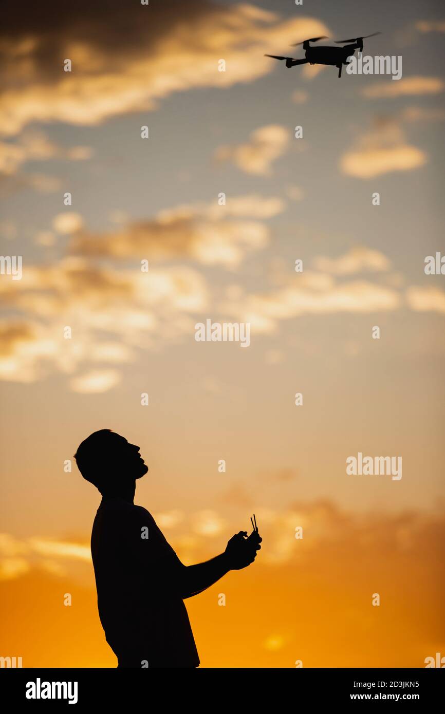 Silhouette eines jungen Mannes, der eine Drohne in EINEM BETRIEB Ländliche Lage bei Sonnenuntergang Stockfoto