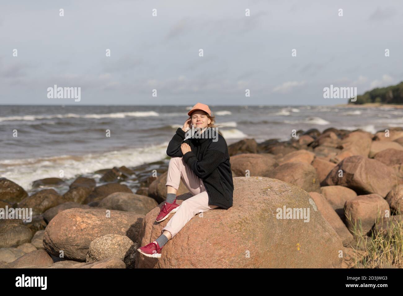 Eine glückliche junge, blonde Frau, die auf einem Felsen sitzt und das Leben genießt Stockfoto