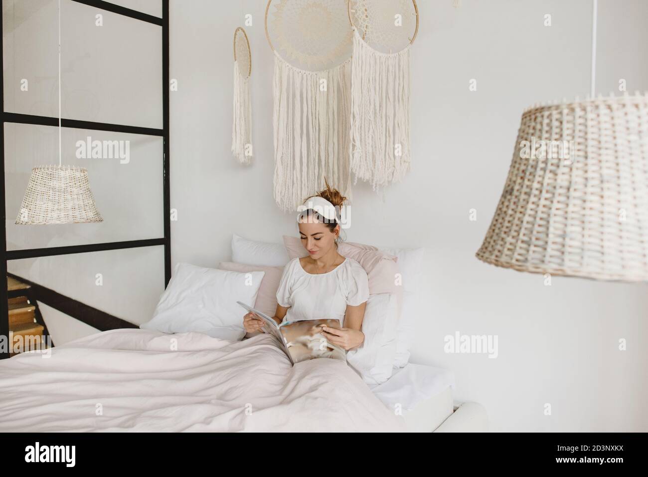 Attraktive Frau liegt im Bett und Lesemagazin. Stockfoto