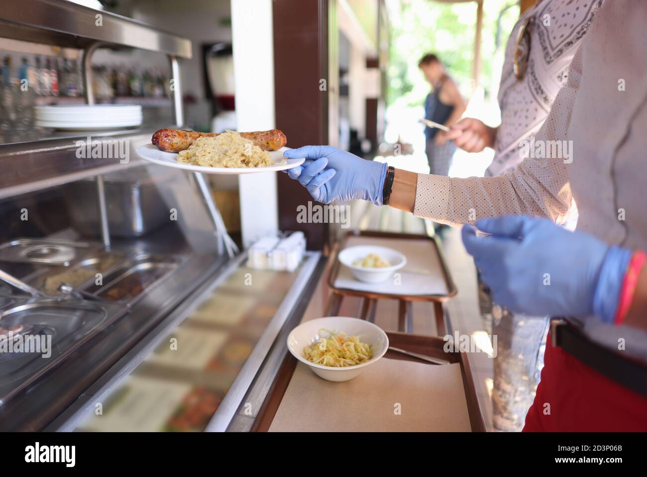 Frau in Schutzhandschuhen im Café nimmt Teller des Essens. Stockfoto
