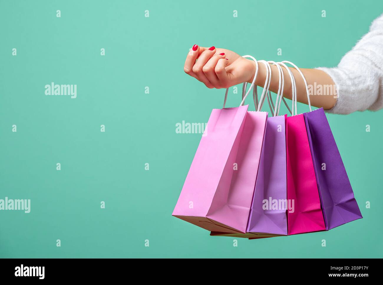 Farbige Papiertüten auf den Händen einer Frau vor blauem Hintergrund. Junge Frau hält an ihrer Hand rosa und lila Einkaufstaschen. Stockfoto