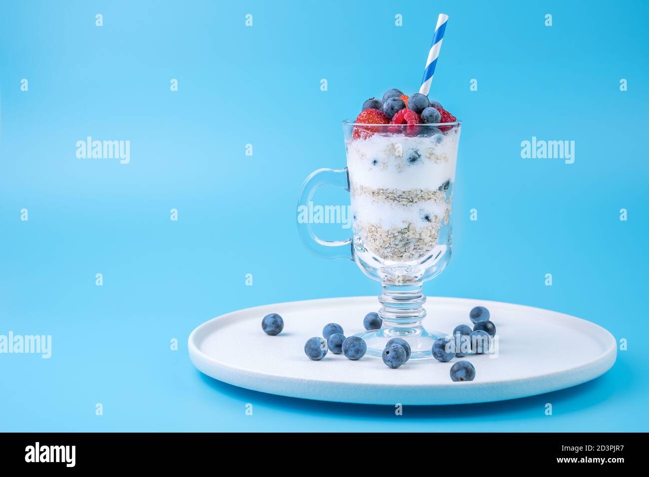 Dessert mit Beeren und Sahne und Getreide auf blauem Hintergrund. Stockfoto