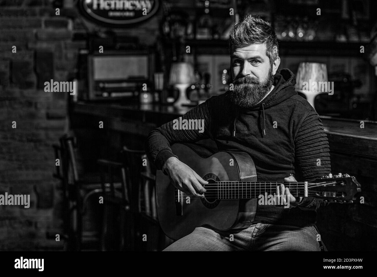 Spielen Sie die Gitarre. Bart Hipster Mann sitzt in einem Pub. Musikkonzept. Bärtiger Gitarrist spielt. Schwarz und Weiß Stockfoto
