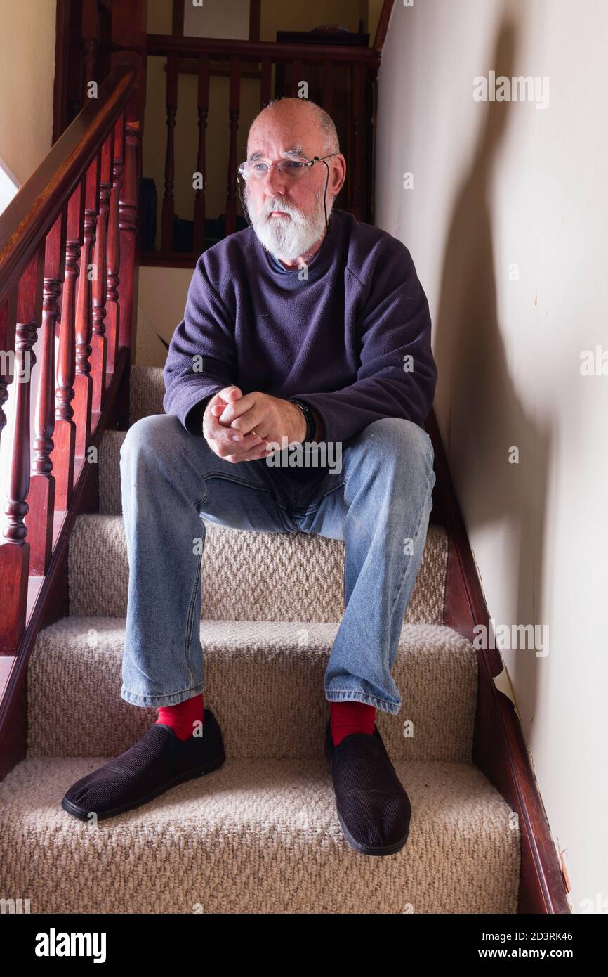 Bärtiger älterer Mann, verloren in Gedanken, sitzt auf der Treppe in seinem alten Haus. Stockfoto