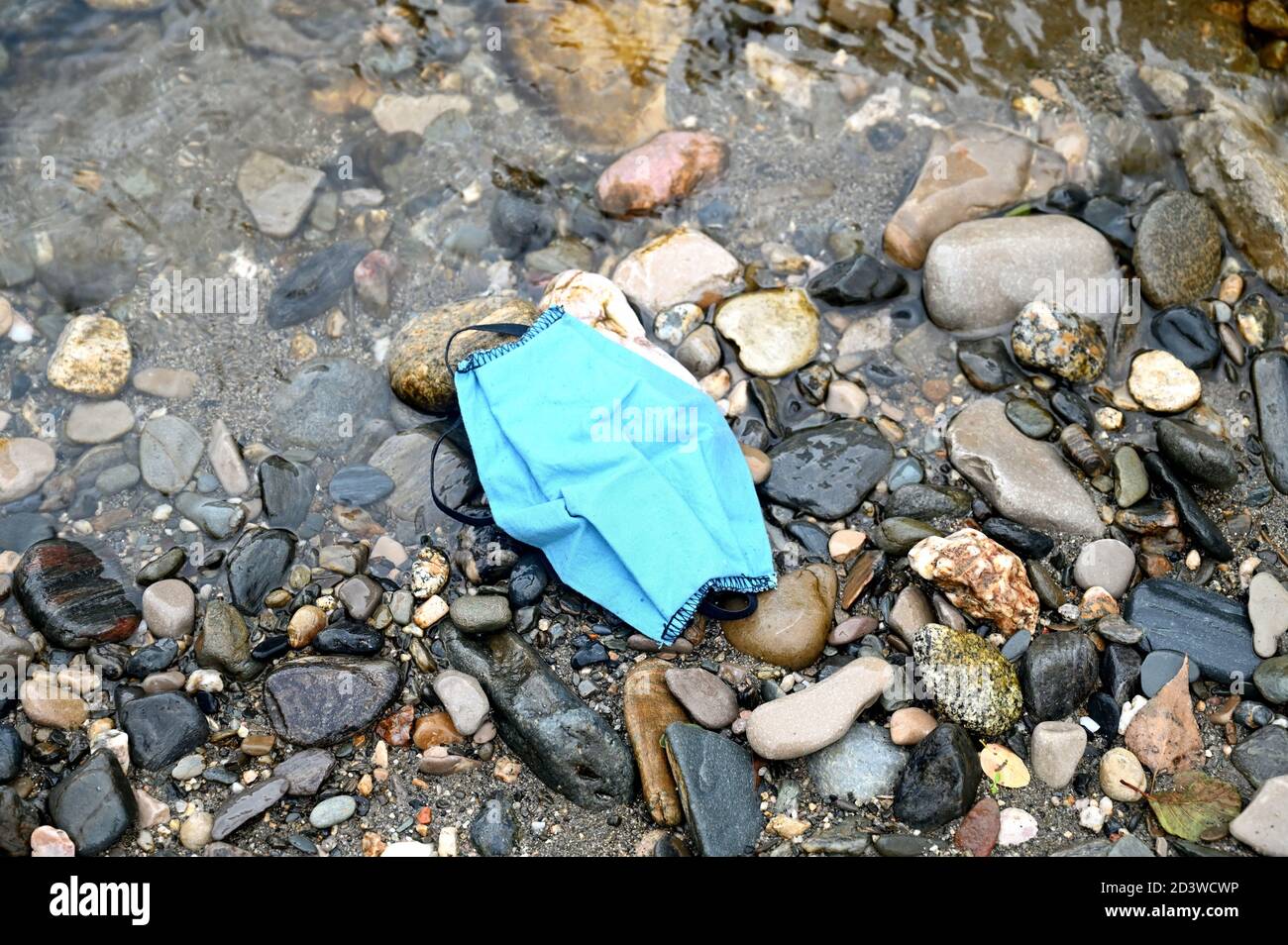 Eine blaue Gesichtsmaske aus Baumwolle wird auf dem abgelegt Strand, wenn es in einen Abfall hätte geworfen werden sollen Behälter Stockfoto