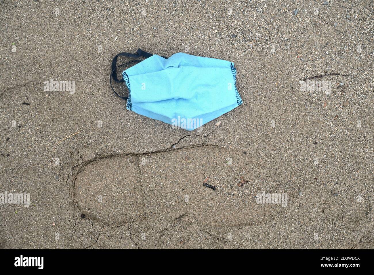 Eine blaue Gesichtsmaske aus Baumwolle wird auf dem abgelegt Strand, wenn es in einen Abfall hätte geworfen werden sollen Behälter Stockfoto