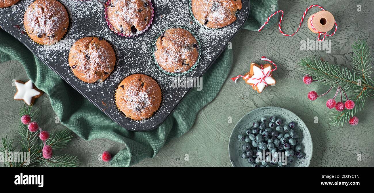 Heidelbeer-Muffins mit Zuckerguss in einem Backblech. Panoramabild von oben mit Weihnachtsdekor Stockfoto