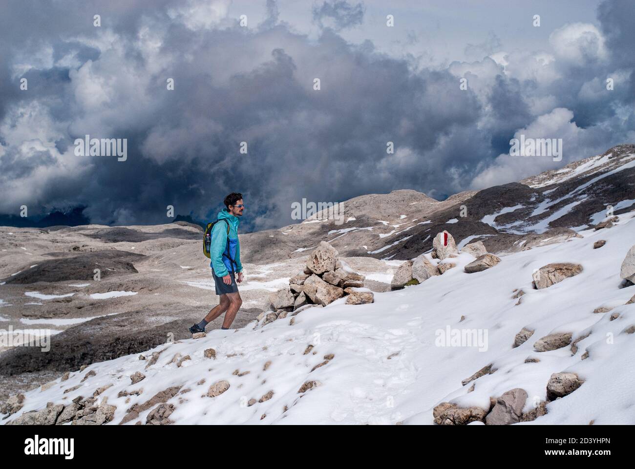 Junger Mann, der an einem bewölkten Tag mit Schnee, kurzen Baumstämmen und Sonnenbrillen auf dem Altipiano delle Pale di San martino von der Hütte Rosetta nach La Fradusta wandert Stockfoto