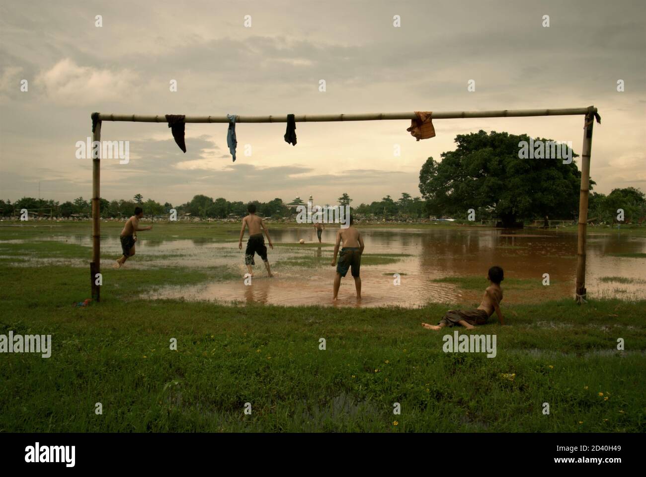 Kinder spielen Fußball auf einem teilweise überfluteten Feld, das sich zwischen zwei öffentlichen Friedhöfen in Pondok Kelapa, Jakarta, Indonesien, befindet. Stockfoto