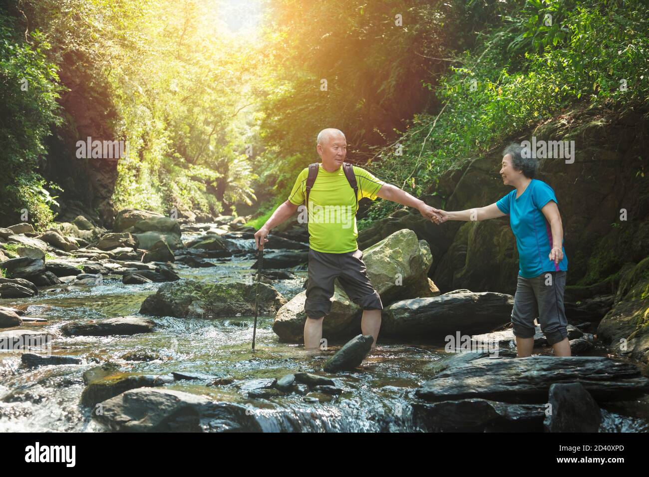 Seniorenpaar, das im Naturpark über einen kleinen Fluss läuft Stockfoto