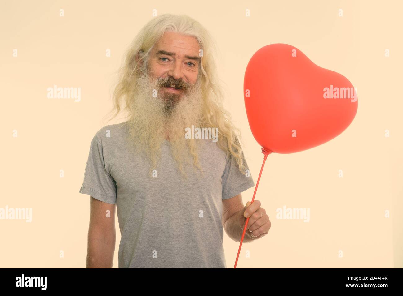 Studio shot von Happy älterer bärtiger Mann lächelnd, während sie rote herzförmige Ballons für den Valentinstag bereit Stockfoto