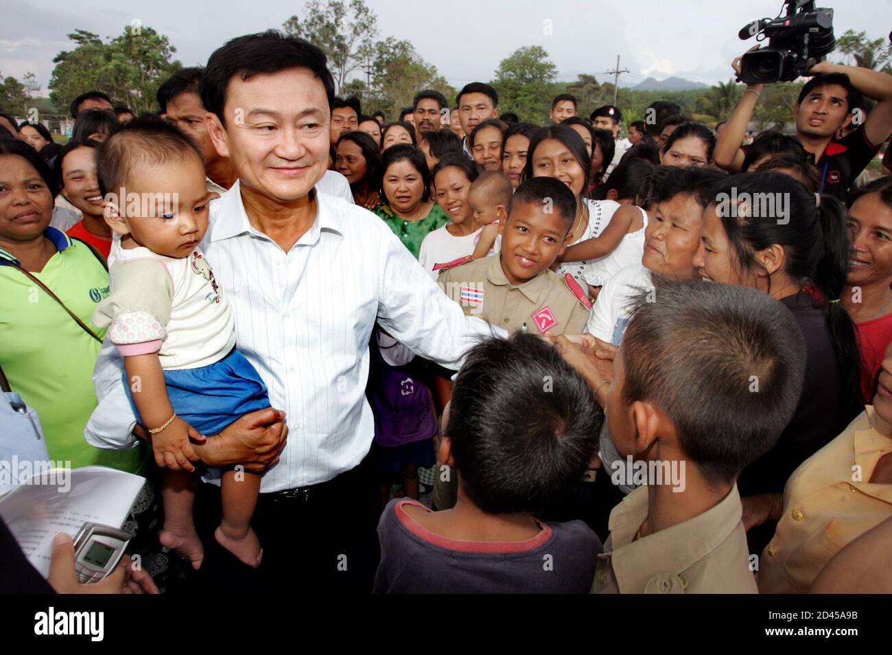Thailändische Premierminister Thaksin Shinawatra trägt ein Kind, wie er Dorfbewohner in Yala Provinz, 1.200 km (750 Meilen) südlich von Bangkok, am 16. Februar 2005 trifft. Thaksin kam in der weitgehend muslimischen Süden am Mittwoch mit eine strenge Botschaft für Dorfbewohner separatistische Kämpfer zu helfen versucht. REUTERS/Sukree Sukplang SS/SA/LA Stockfoto