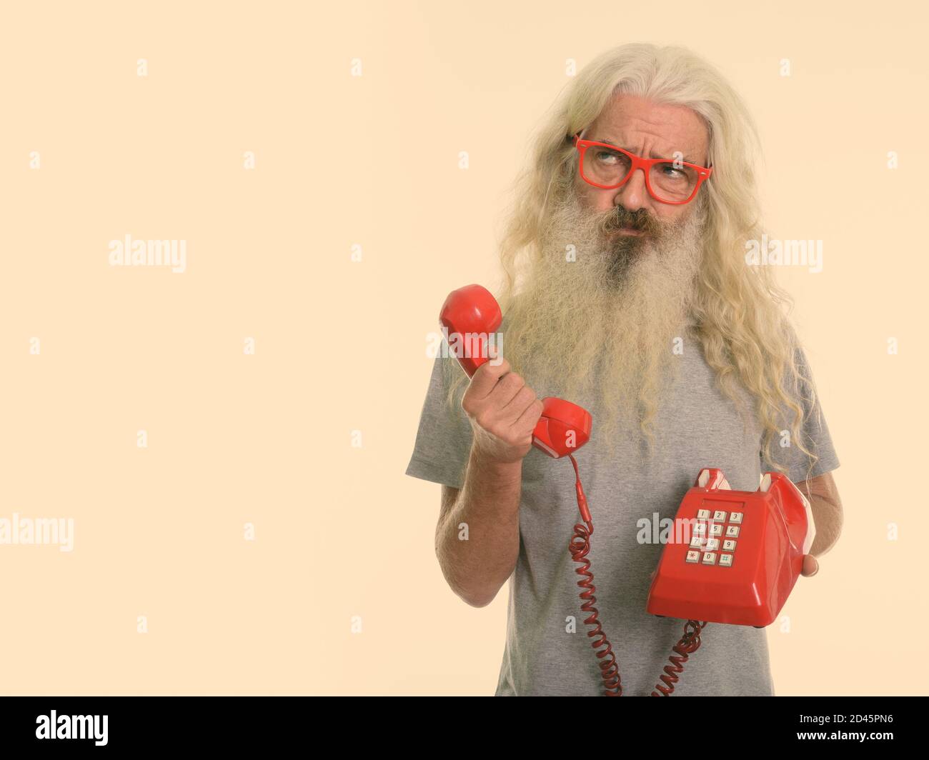 Studio shot der älteren bärtigen Mann mit alten Telefon beim Denken und Suchen Stockfoto