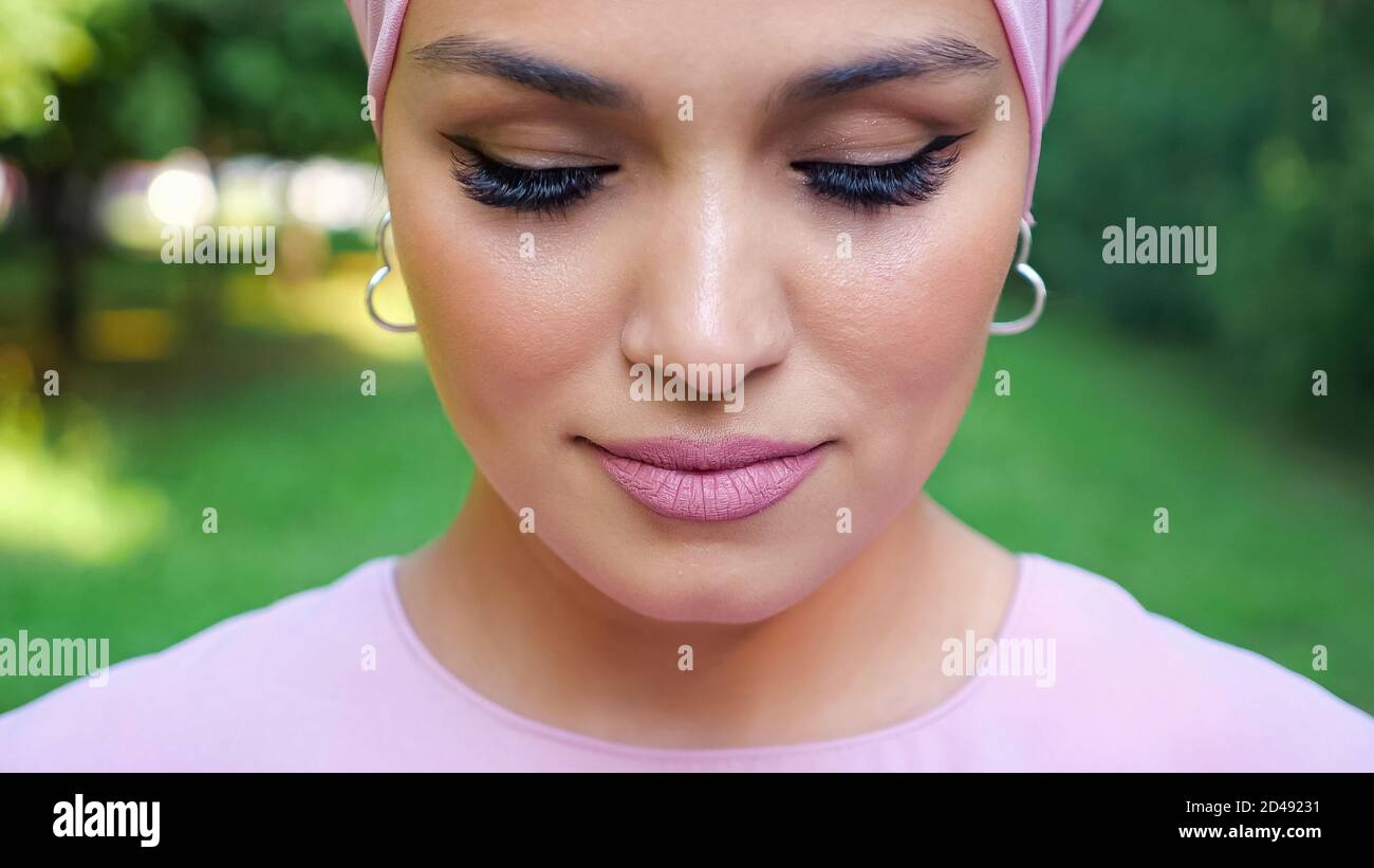 Modische Frau mit silbernen Ohrringen und lila Hijab mit geschlossen Augen stehen gegen verschwommene Park Nahaufnahme Stockfoto