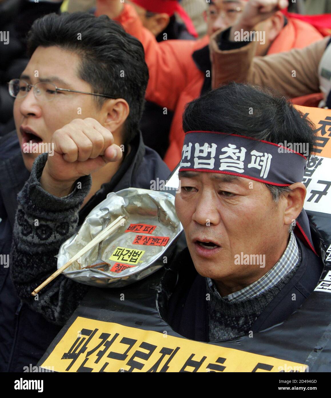 Tragen die mock Bestände und eine Schüssel mit Stäbchen und Löffel, Gesänge eine südkoreanische Zeitarbeitnehmer Anti-Regierungs-Sloagns bei einer Kundgebung in der Nähe von Parlament in Seoul 24. November 2004. Etwa 400 gewerkschaftlich organisierten Leiharbeitnehmer sammelten in Seoul am Mittwoch ein Regierung-driven Gesetz widersetzen, die sie darauf bestehen, ihre Arbeitsbedingungen verschlechtern würde. REUTERS / Sung-Ho-YSH/SH Stockfoto