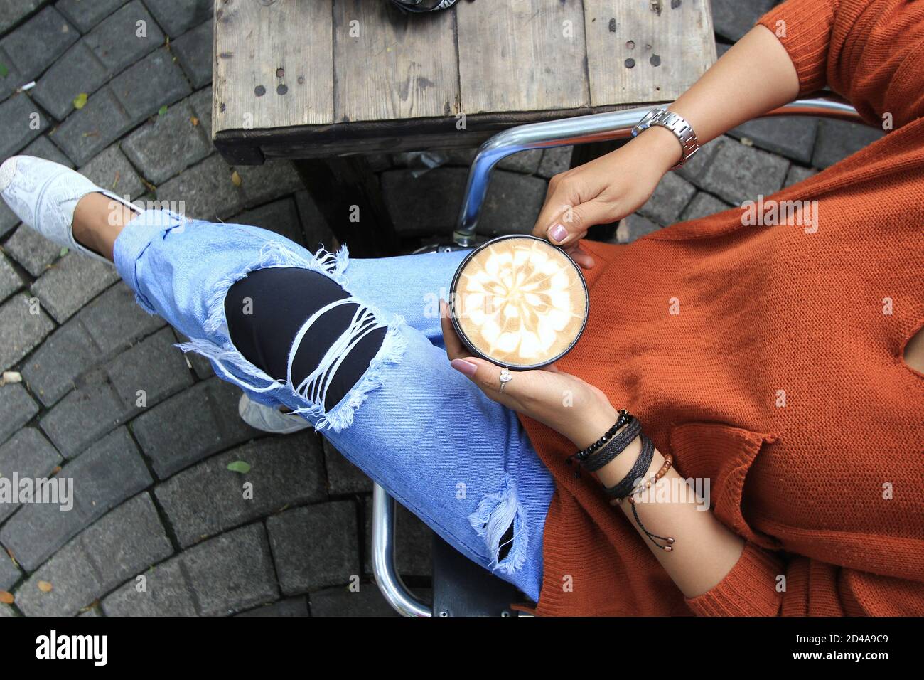 Eine Frauenhand hält Latte Art Kaffee auf einem Holztisch. Jemand genießt Kaffeepausen während des Tages Stockfoto