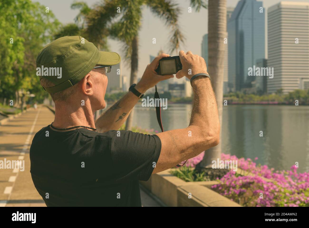 Senior touristische Mann mit Kappe während Bilder im ruhigen Park in Bangkok, Thailand, Stockfoto