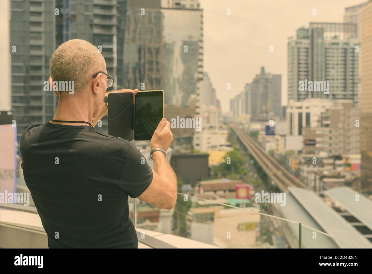 Rückansicht des kahlen Senior touristische Mann mit digitalen Tablet die Ansicht der Stadt in Bangkok, Thailand Stockfoto