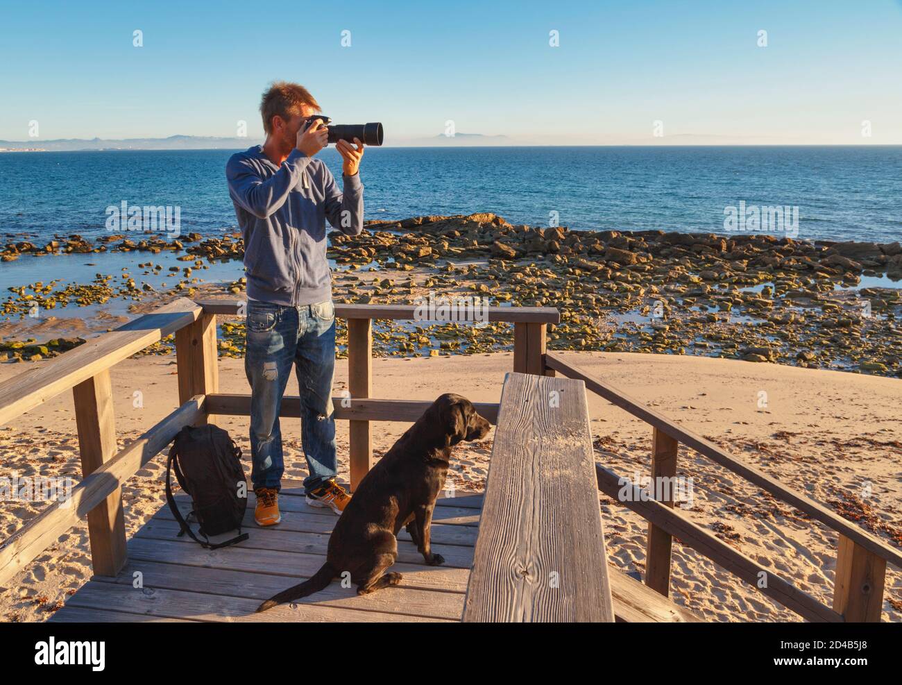 Ein Fotograf komponiert ein Bild. Auch sein Hund schaut auf das Thema. In der Nähe von Tarifa, Costa de la Luz, Provinz Cadiz, Andalusien, Südspanien. Stockfoto