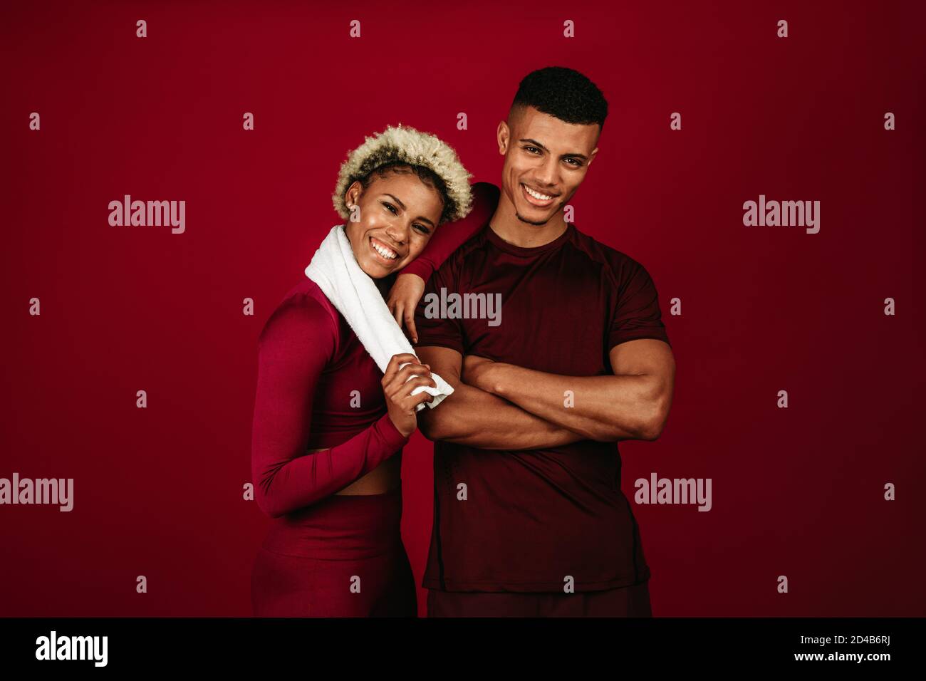 Fröhliches afroamerikanisches Paar in Fitnesskleidung, das zusammen auf kastanienbraunem Hintergrund steht. Fitnesspaar, das sich nach dem Training entspannt. Stockfoto