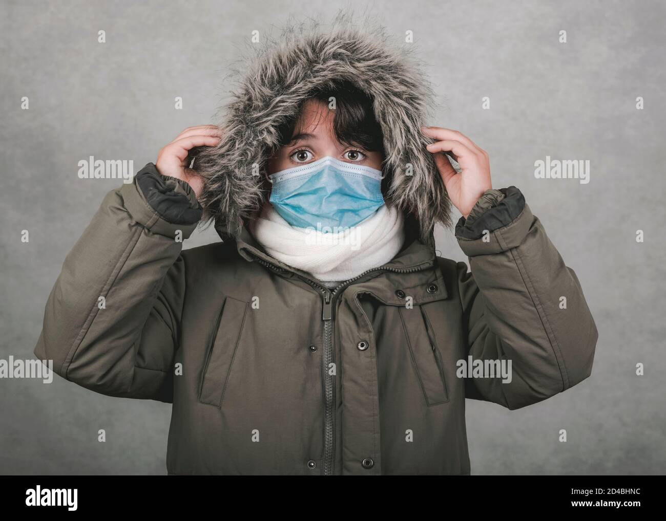 Kind mit medizinischer Maske trägt Winterhut und Schal über Grauer Hintergrund Stockfoto