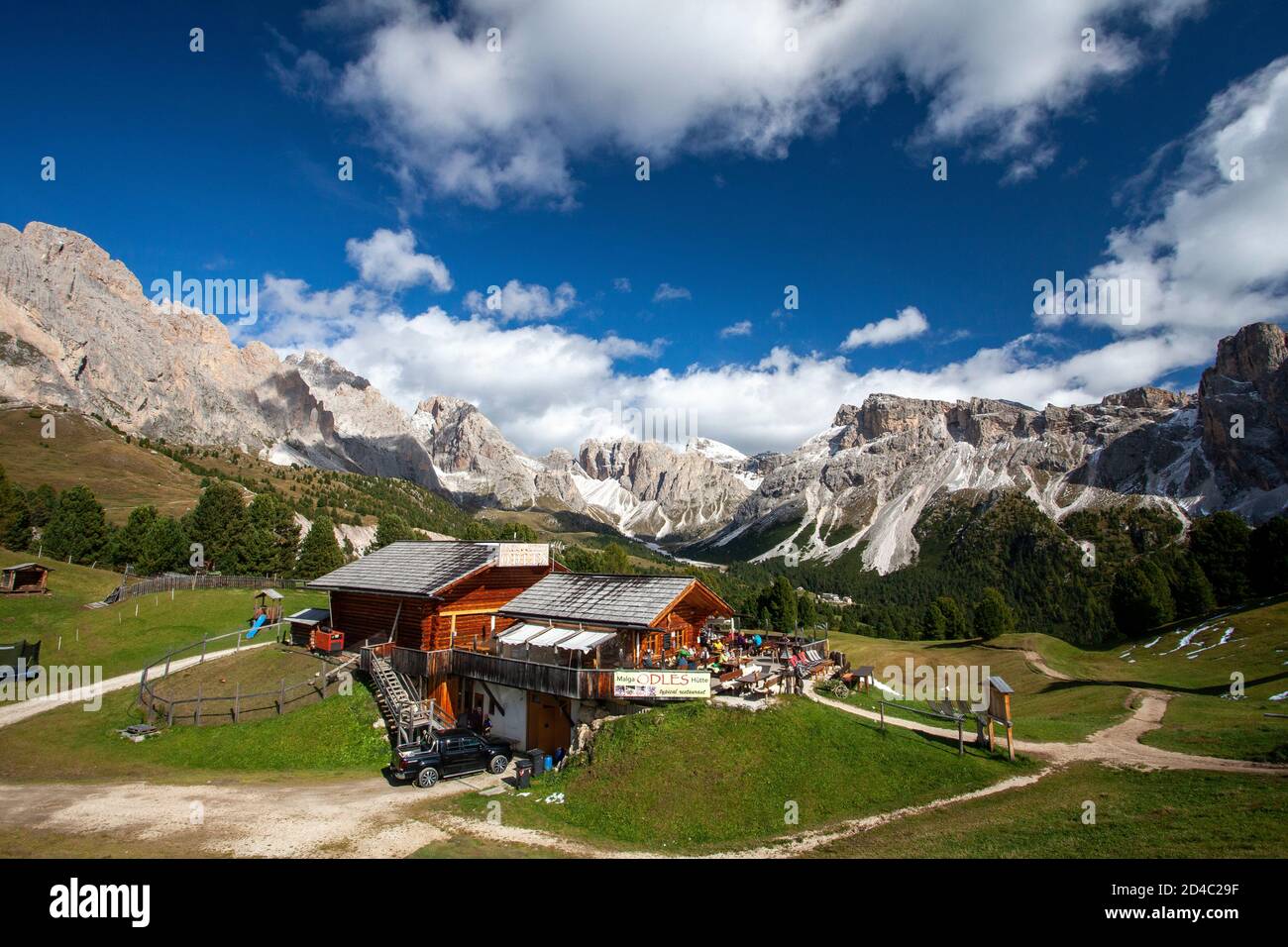 Die Baita Odles Rifugio/ Hütte Ist offen für Geschäfte unter blauem Himmel mit einem atemberaubenden Hintergrund der Geisler Gruppe von Dolomitengipfeln Stockfoto