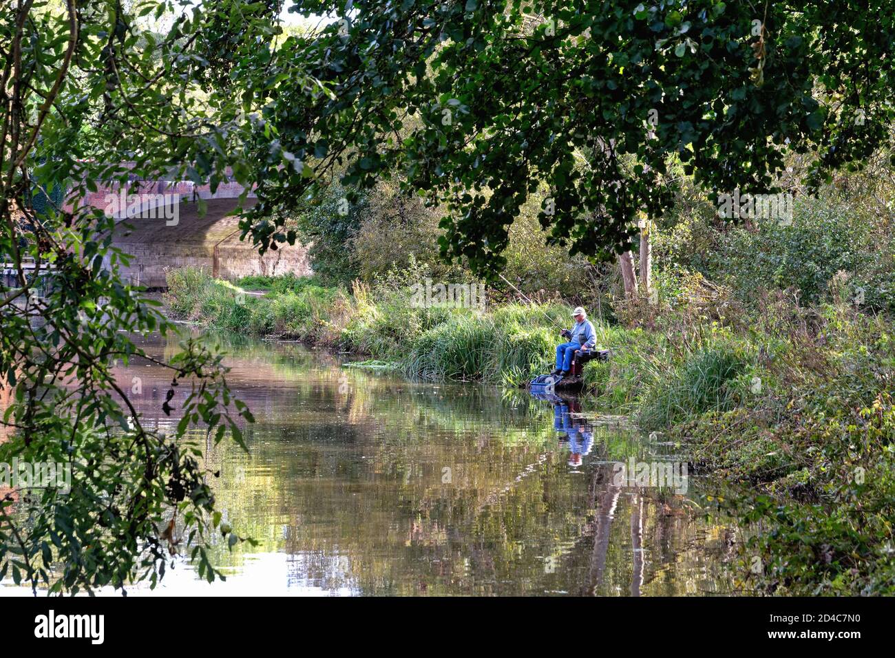 Ein älterer männlicher Fischer, der am Flussufer auf dem sitzt River Wey Schifffahrtskanal bei Weybridge Surrey England Stockfoto