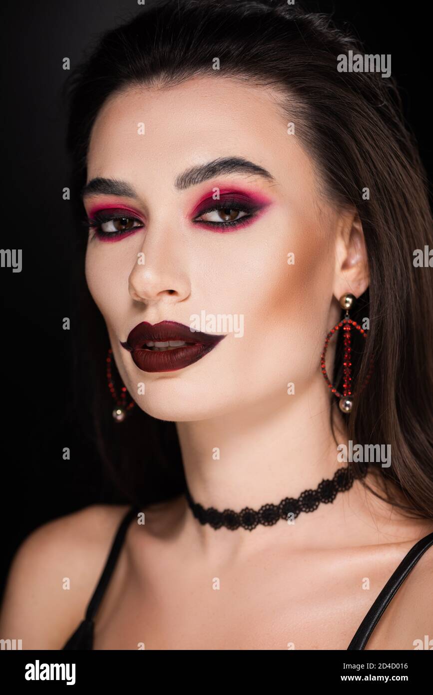 Junge Frau mit dunklem Make-up und Zubehör Blick auf Kamera Isoliert auf Schwarz Stockfoto