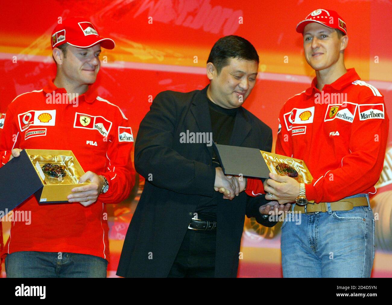 Ferrari's siebenfacher Formel-1-Champion Michael Schumacher (R) erhält ein Geschenk von Yu Zhifei, Deputy General Manager of Shanghai Circuit, während Teamkollege Rubens Barrichello (L) nach einer Pressekonferenz in Shanghai am 22. September 2004 betreut. Shanghai wird am 26. September den ersten chinesischen Grand Prix mit einer atemberaubenden Strecke und einem Ausverkauf von mindestens 150,000 Zuschauern ausrichten. Einer von zwei Grand prix-Debüts in diesem Jahr - der andere war Bahrains erstes Rennen im Nahen Osten -, die es der Formel 1 ermöglichen, sich als eine wahrhaft globale Meisterschaft zu rühmen. REUTERS/Claro Cortes IV CC/SH Stockfoto