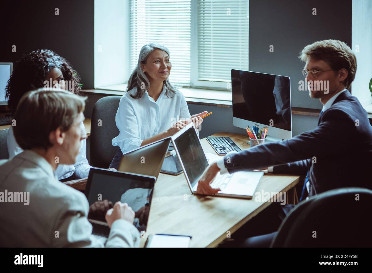 Vielfältiges kreatives Team, das am großen Tisch mit Computern arbeitet. Brainstorming von Büromitarbeitern. Hochwertige Fotos Stockfoto