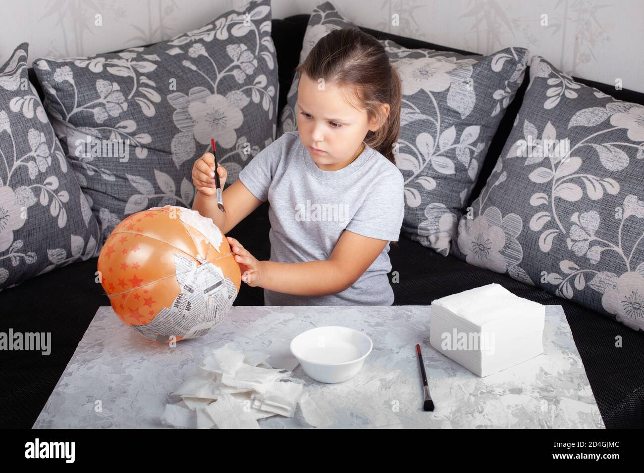 Ein Kind sitzt auf dem Sofa und macht einen Pappmaché Kürbis für Halloween aus einem Ballon Stockfoto