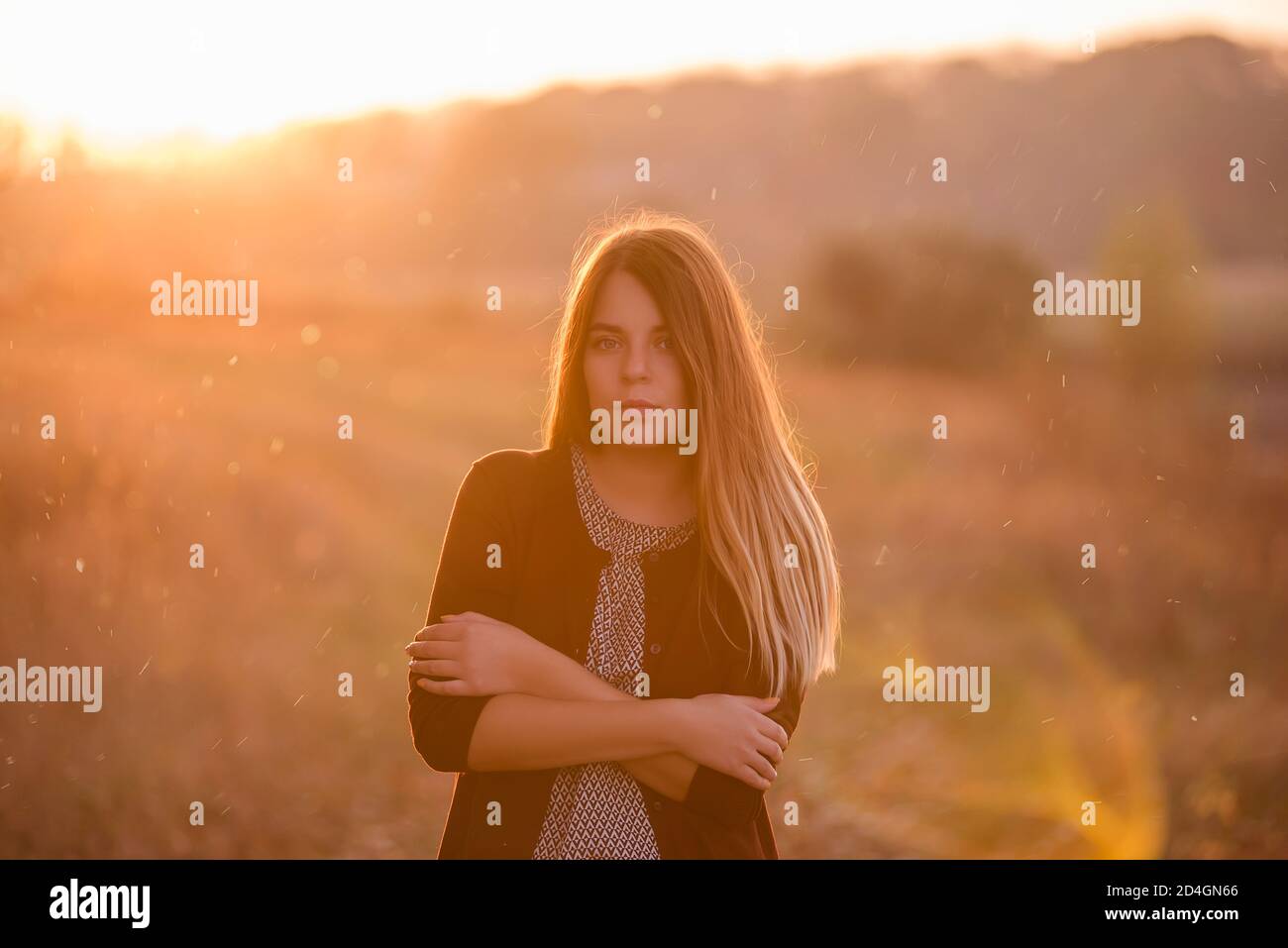 Ein modernes, schönes Mädchen, in einer burgunderroten Jacke, dunkle Jeans, steht in einem Feld, blonde Haare flattern im Wind vor dem Hintergrund eines Herbstes Stockfoto