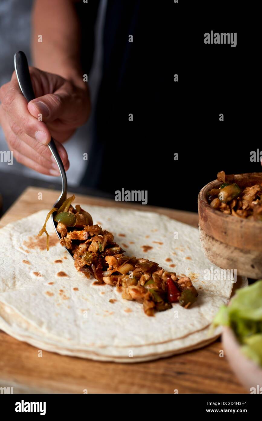 Nahaufnahme eines jungen kaukasischen Mannes, der ein Durum oder Burrito zubereitet, mit Hühnerfleisch und gekochter Zwiebel, rotem Pfeffer und grünem Pfeffer Stockfoto
