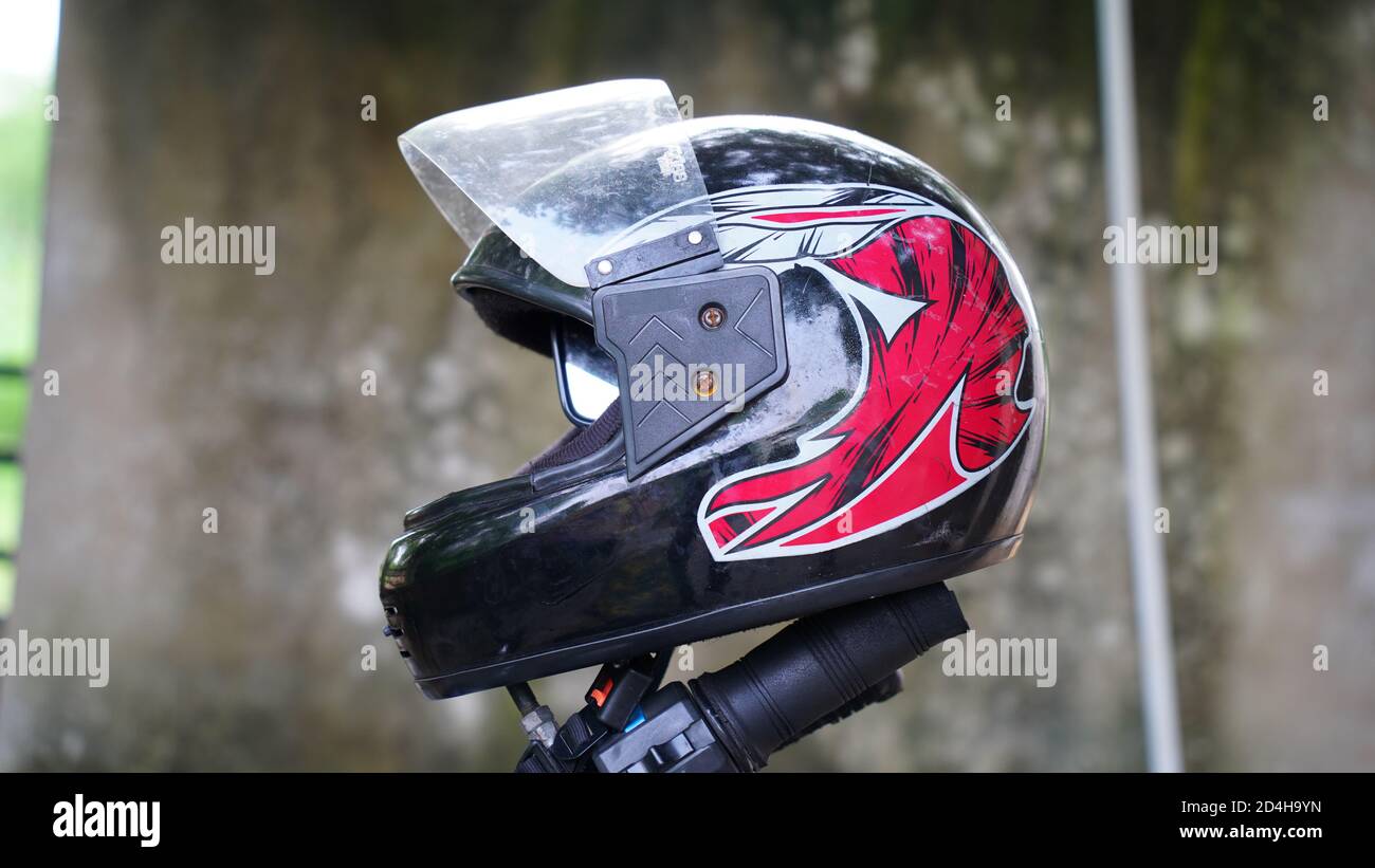 Ein farbenfroher Helm, der auf einem Motorradgriff montiert ist. Alter Helm mit verschwommenem Hintergrund. Stockfoto