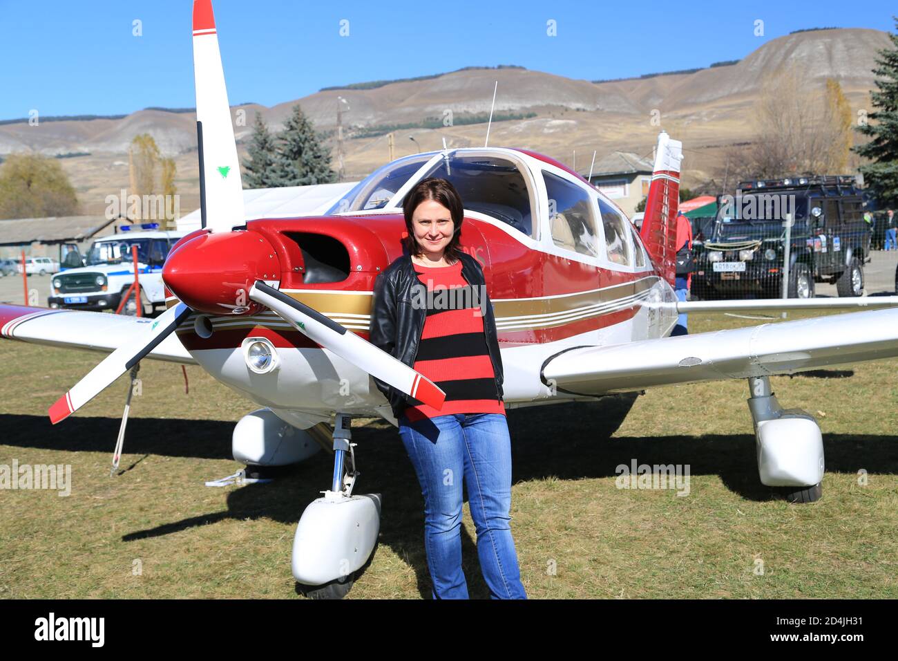 Eine junge Frau steht bei einer Flugshow mit einem Lächeln neben einem Flugzeug. Stockfoto