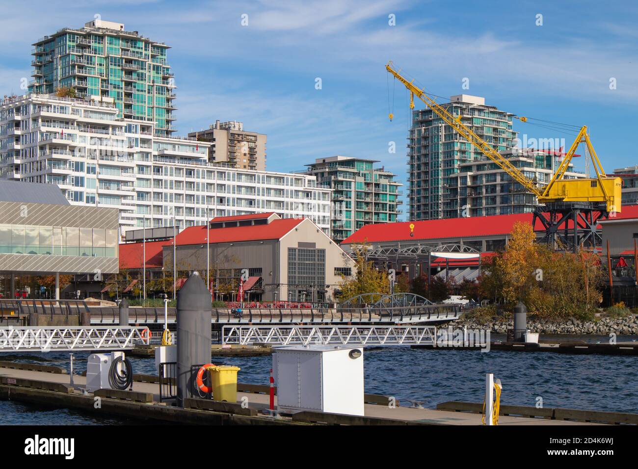 Hafenpromenade mit Hafenblick. Moderne Wohnhäuser mit großem gelben Kran. North Vancouver (British Columbia, Kanada) Quay. Stockfoto