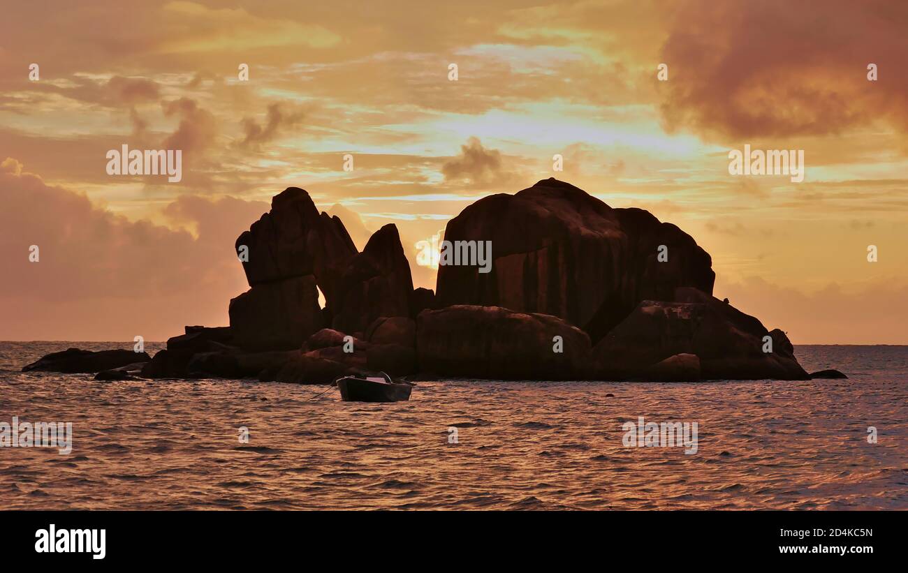 Schöner Sonnenuntergang mit orangefarbenem Himmel mit Granitfelsen im Meer und einem Andockboot vor der Küste von Praslin, Seychellen. Stockfoto