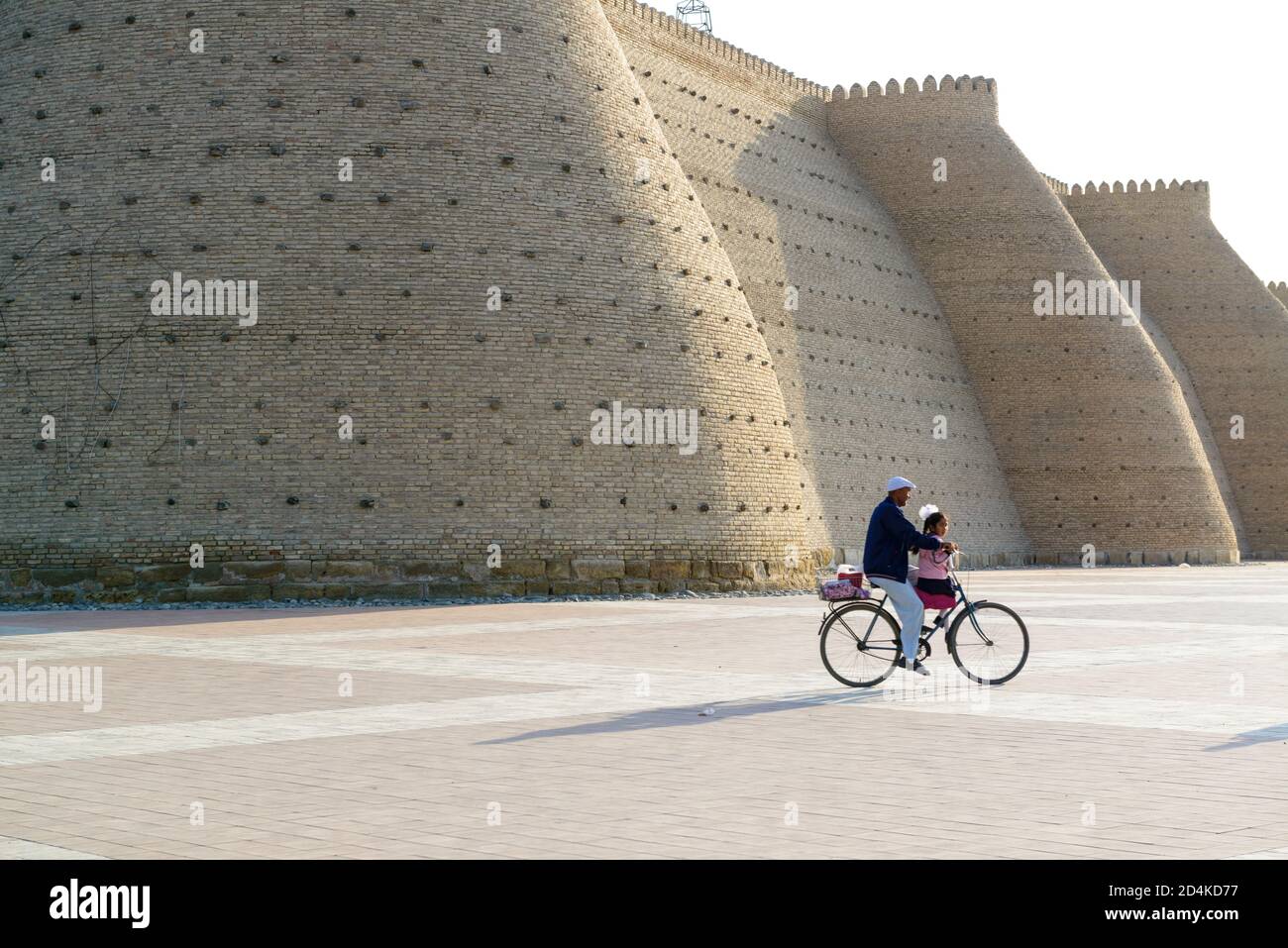 Vater und Tochter radeln entlang der Mauern der Arche von Buchara. Buchara, Usbekistan, Stockfoto
