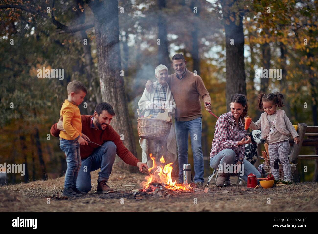 Eine glückliche Familie und ihr Hund genießen wunderbare Zeit um Lagerfeuer im Wald an einer schönen Herbstdämmerung Stockfoto