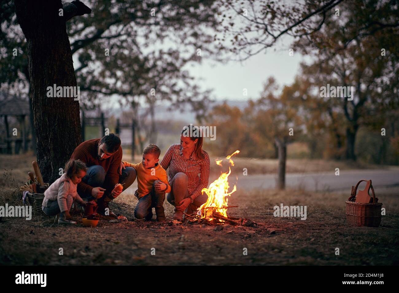 Eine glückliche Familie, die gemeinsam am Lagerfeuer im Wald genießt An einer schönen Herbstdämmerung Stockfoto