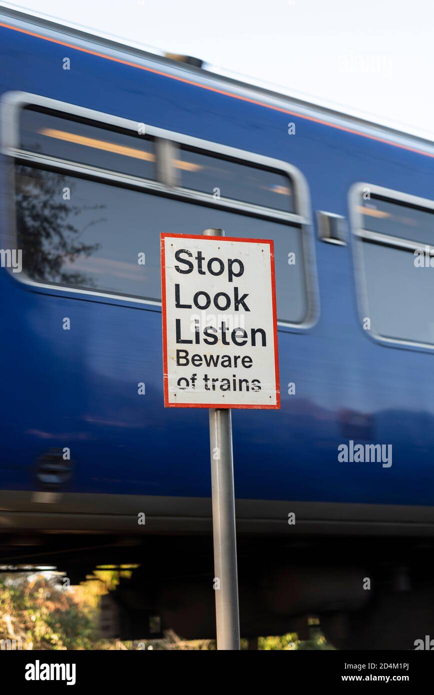 Vorsicht vor den Zügen. Halten Sie an, schauen Sie, hören Sie Warnschild am Bahnübergang mit Greater Anglia Zug vorbei Hawkwell, Rochford, in der Nähe von Southend, Essex, Großbritannien Stockfoto