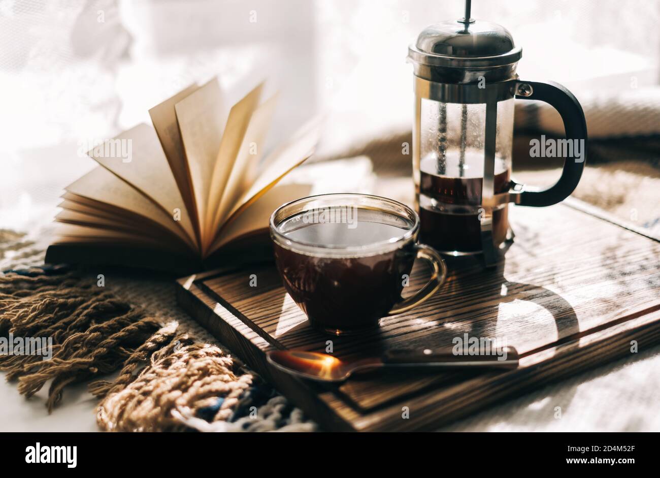 In einer französischen Presse gebrühter Kaffee und eine Tasse auf einem Brett mit Buch auf einem Tisch. Stockfoto