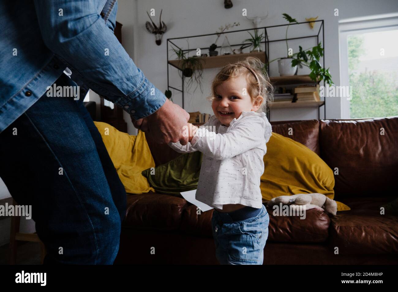 Nette kleine Tochter kichernd, während Vater mit ihr im Wohnzimmer tanzt. Stockfoto