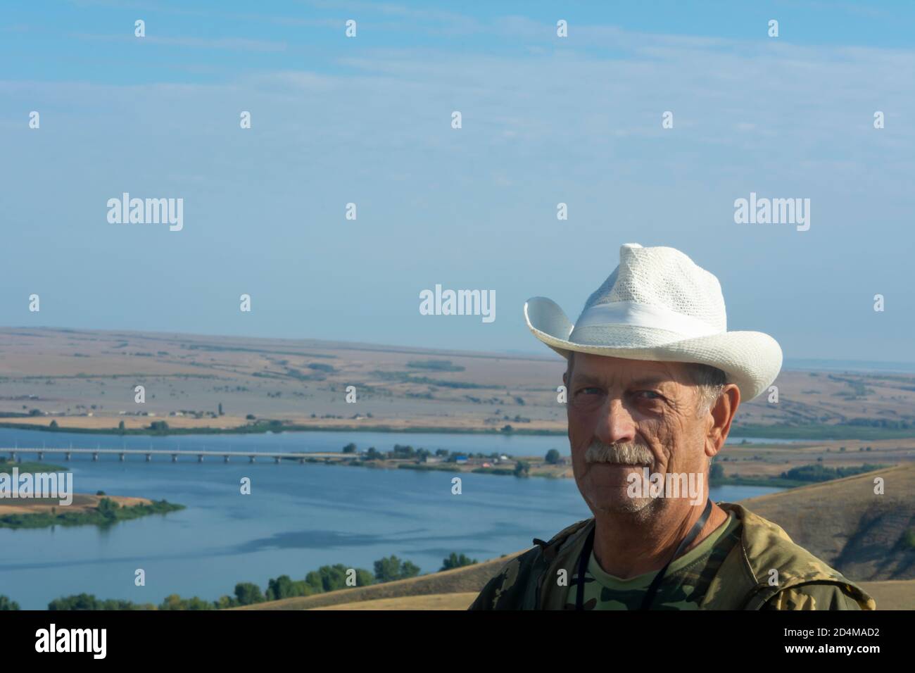 Porträt eines älteren Mannes im Hut. Ein älterer Mann steht auf dem Berg, unten gibt es einen Fluss und eine schöne Landschaft. Lifestyle-Konzept für Senioren. Stockfoto