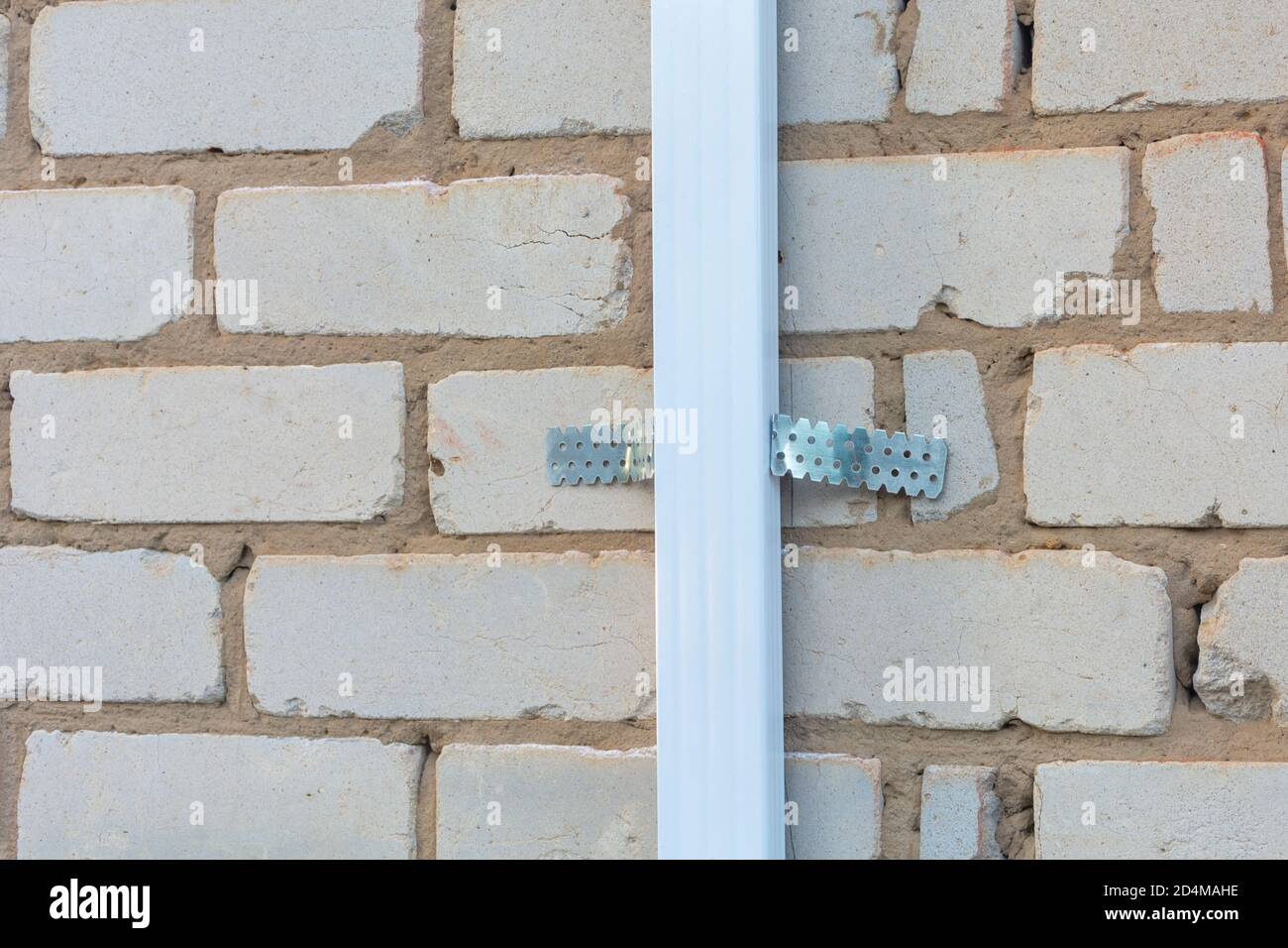 Die Befestigung des Aluminiums für das metallische Profil auf der Fassade der Ziegelwand des Hauses. Bau, Renovierung und Dekoration draußen. Nahaufnahme. Stockfoto