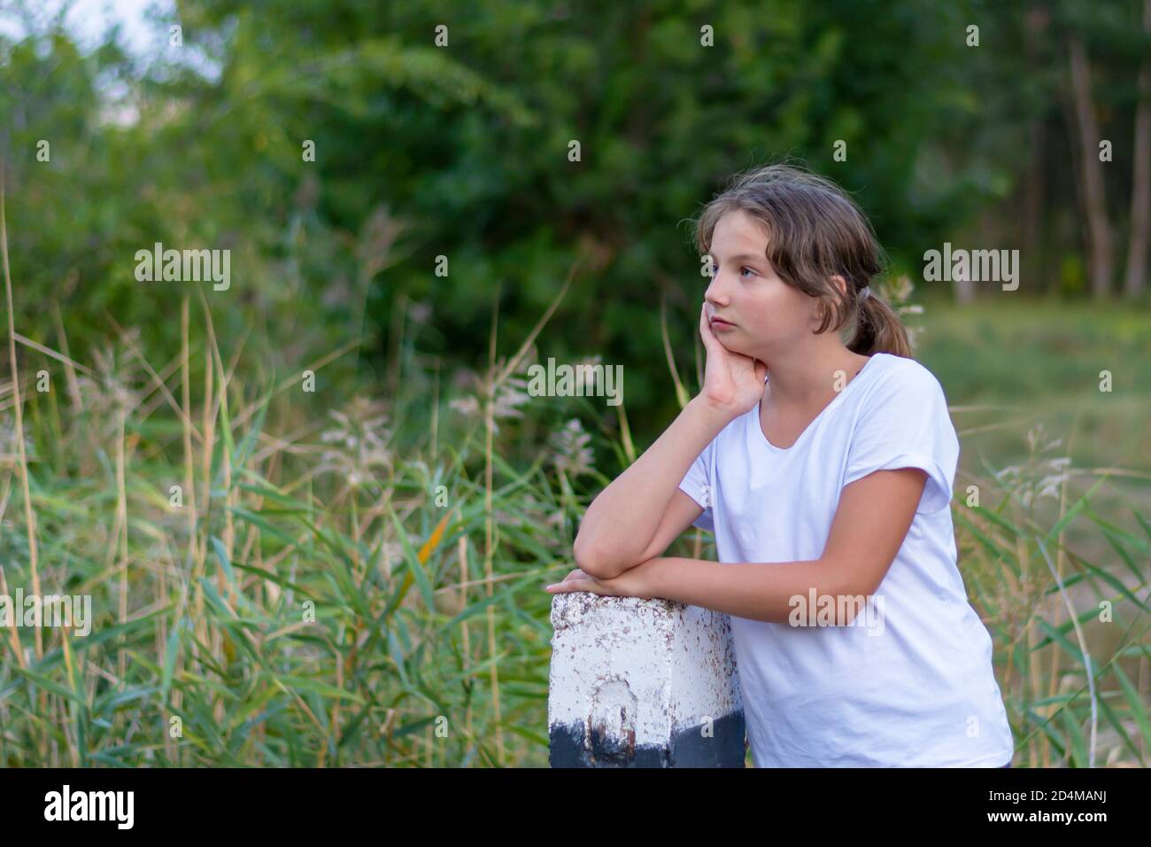 Ein schönes Mädchen im Teenageralter in weißen Kleidern im Wald sieht zur Seite. Portrait im Park im Freien. Emotionen, Gefühle Konzept. Stockfoto