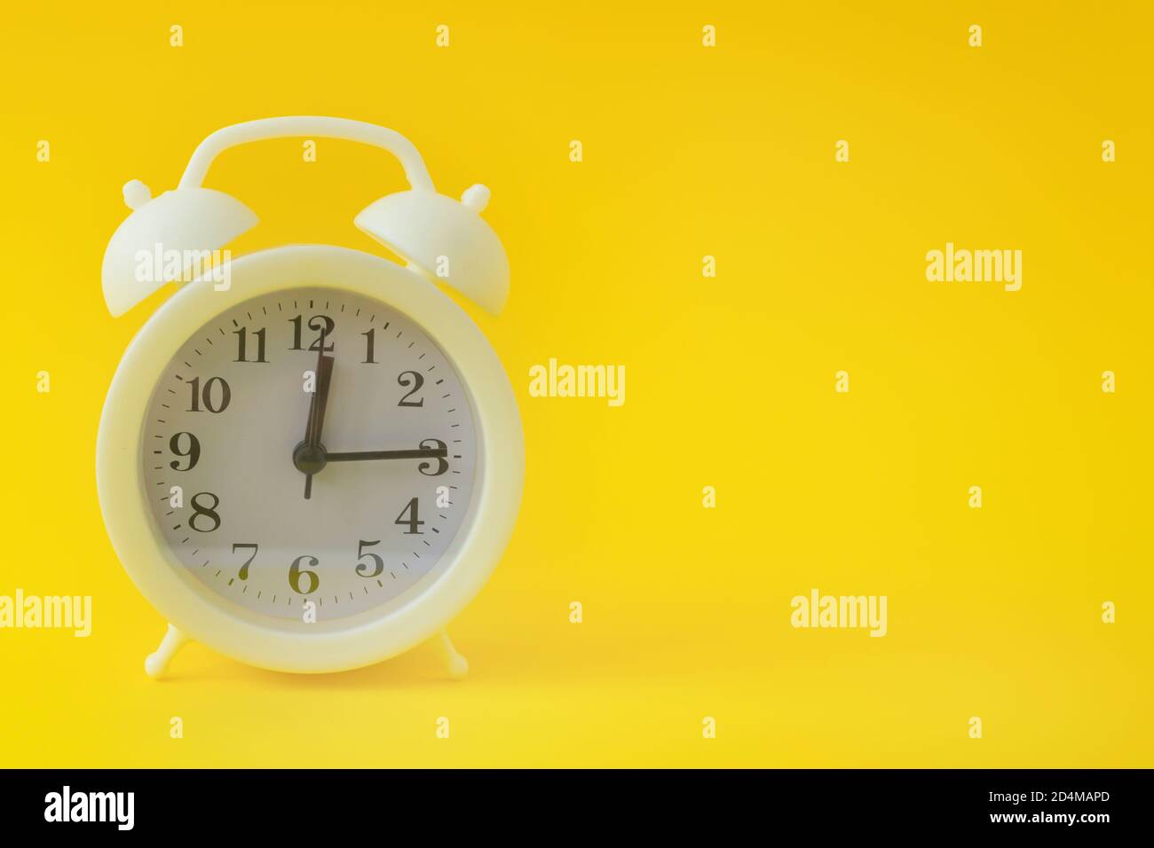 Weißer Vintage-Wecker auf hellgelbem Hintergrund. Uhr mit schwarzen Pfeilen. Platz kopieren, Banner. Stockfoto