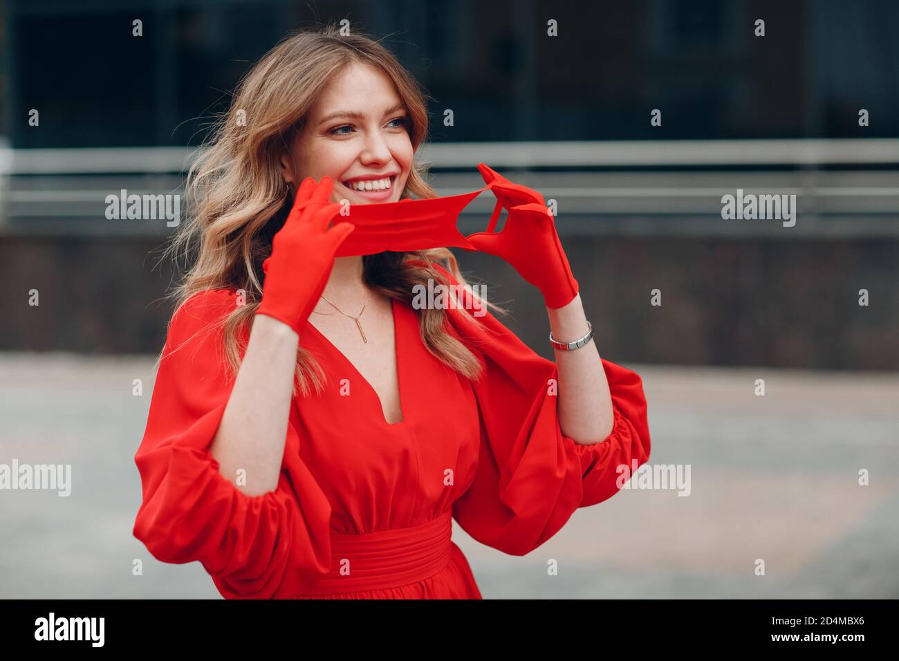 Junge Frau in rotem Kleid und Handschuhe anziehen medizinische Potective Gesichtsmaske Stockfoto